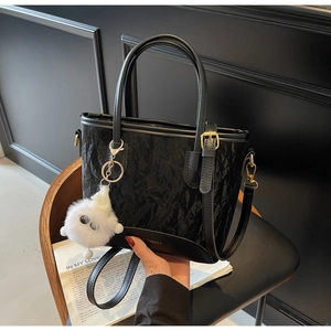 Détail d'un sac seau plissé noir avec breloque peluche et bordure en cuir de luxe
