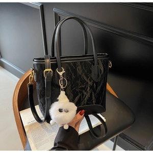Gros plan d'un sac seau noir plissé avec pendentif en peluche sur un siège en bois sombre