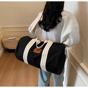 Detail of large black canvas travel bag with white straps and leather logo patch