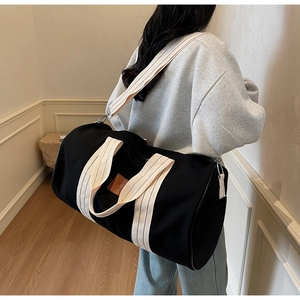 Detail of black travel bag with cream straps shown in a minimalist interior scene