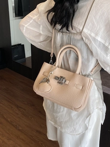 Beige pebble leather bucket bag with silver twist lock and heart pendant accessory