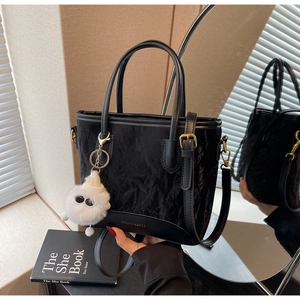 Détail d'un sac cabas plissé noir avec ferrures dorées et breloque en peluche