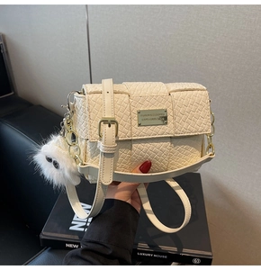 Details einer weißen geflochtenen Handtasche mit goldenen Beschlägen und Anhänger