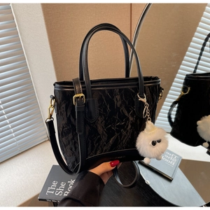 Détail du sac seau noir plissé avec boucles dorées et pendentif en peluche blanche