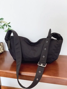 Large black pleated crescent hobo bag with adjustable wide strap on a wooden table