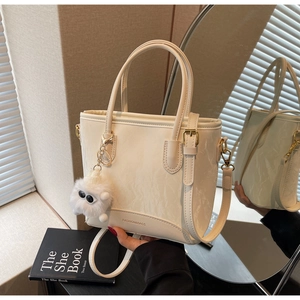 Détail du sac cabas crème avec texture marbrée, finitions dorées et breloque pompon monstre