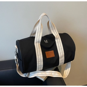 Detail of black cylinder travel bag with cream striped straps and leather logo patch