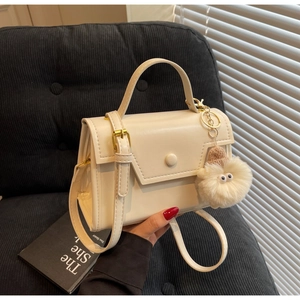 Dettaglio di una borsa quadrata in pelle bianco crema con fibbia tonda e pompon