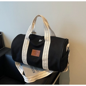 Macro shot of large black canvas travel bag with striped handles on a leather sofa