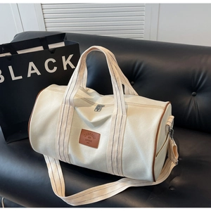 Detail view of cream canvas travel bag with brown leather trim on a black sofa
