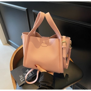 Sac seau rose en cuir grainé avec lettrage doré posé sur un fauteuil en cuir noir chic