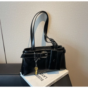 Detail of black glossy shoulder bag with woven strap and yellow key pendant accessory