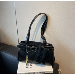 Detail of black glossy PU leather tote bag with decorative buckle and yellow key pendant