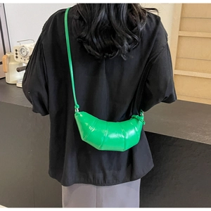 Detail of a bright green croissant crossbody bag with pleated texture on a female model