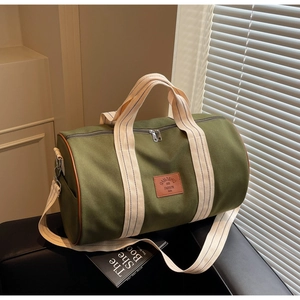 Detail of green canvas travel bag with striped handles and leather label on black bench