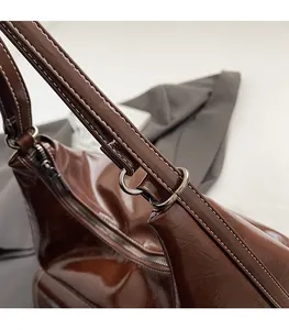 Détail du sac en cuir verni marron foncé avec coutures blanches et anneau en D argenté