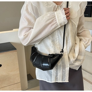 Side view of black leather croissant bag with segmented stitching and slim shoulder strap
