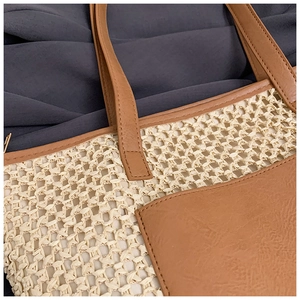 Detailed close-up of handmade woven straw tote bag with brown leather pocket and stitching
