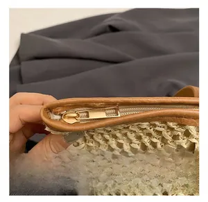 Detailed close-up of light gold metal zipper and brown leather trim on straw bag