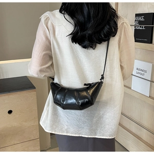 Detail of a black shiny croissant bag with 3D panelled design and knotted shoulder strap
