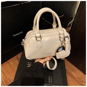 Close-up of cream Boston bag with heart charm, leather texture, and shoulder strap