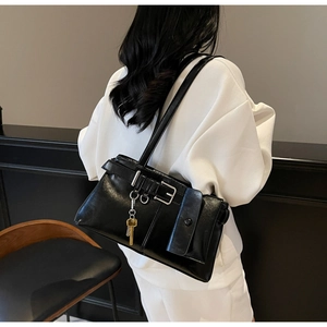 Detail of black glossy shoulder bag with belt buckle and metallic key pendant detail