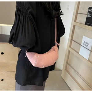 Detail of pink croissant shoulder bag with sleek leather texture on female model