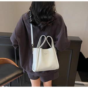 Détail du sac seau gris en cuir grainé avec bandoulière et logo gaufré sur le devant
