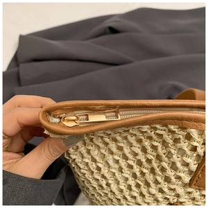 Detailed macro view of the golden metal zipper and brown leather trim on the straw tote bag