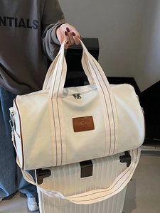 Cream canvas duffle bag with brown leather accents on a white suitcase for travel