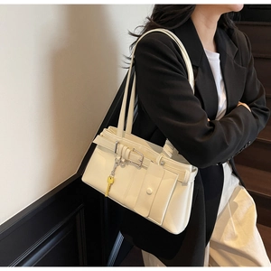 Detail of minimalist beige faux leather shoulder bag with yellow key pendant and metal buckle