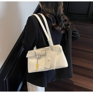 Detail of cream white shoulder bag with decorative belt, mini pouch and yellow key pendant