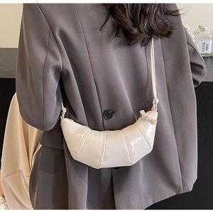Detail of off-white glossy croissant bag featuring segmented stitching and side knot detail