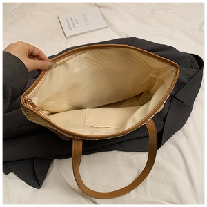 Detail view of woven straw tote bag with brown leather handles and zippered inner lining