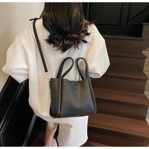 Détail du sac seau noir à motif litchi avec ferrures dorées et bandoulière chic