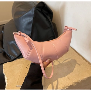 Detail of a pink crescent-shaped leather bag with segmented stitching and side knot accents