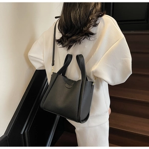 Gros plan d'un sac seau en cuir noir à motif litchi porté par un mannequin dans une pièce