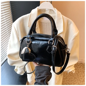 Detail of a shiny black Boston bag featuring silver heart charm and leather texture