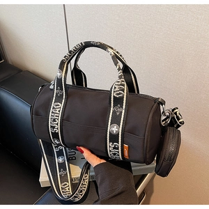 Détail d'un sac cylindrique en nylon noir avec bandoulière à lettres et pochette amovible