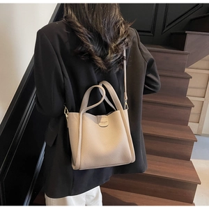 Sac seau en cuir grainé beige avec poignée et bandoulière présenté en contexte lifestyle