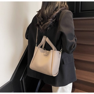 Détail du sac seau en cuir grainé taupe avec des ferrures dorées élégantes et bandoulière