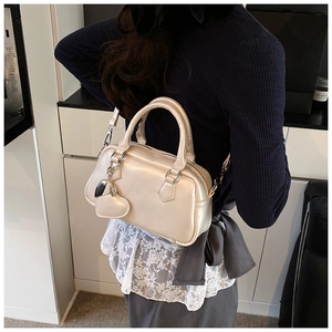 Detail of champagne gold Boston bag with heart charm and silver hardware on a model