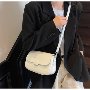 Close-up of minimalist white leather crossbody bag with flap and metal strap hooks
