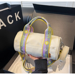 Détail d'un sac cylindre en toile avec bandoulières tissées et petit porte-monnaie rond