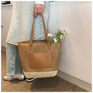 Detail of woven straw tote bag featuring brown faux leather pocket and shoulder strap