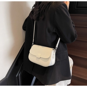 Close-up of a creamy beige crossbody bag styled with a minimalist black blazer