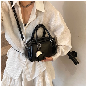Detail of black patent leather mini boston bag with silver heart charm and crossbody strap