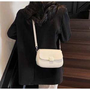 Detail of a minimalist cream saddle bag with square buckle worn with a black blazer