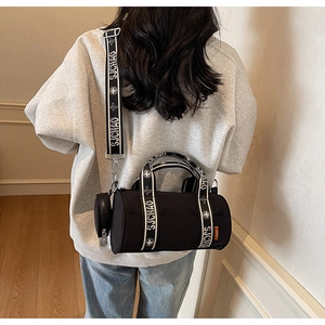 Détail d'un sac bandoulière cylindrique noir avec des sangles griffées et un porte-monnaie