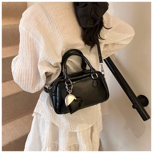 Close-up of black patent leather bowling bag with heart charm and crossbody strap